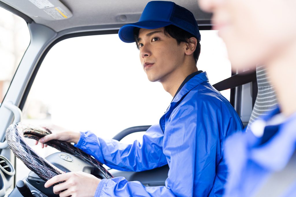 トラックを運転する青いジャンパーを着た男性